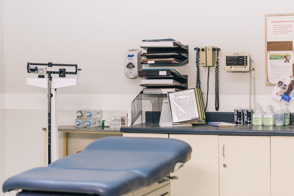 Well-equipped medical examination room with exam table, physician scale, and organized supplies