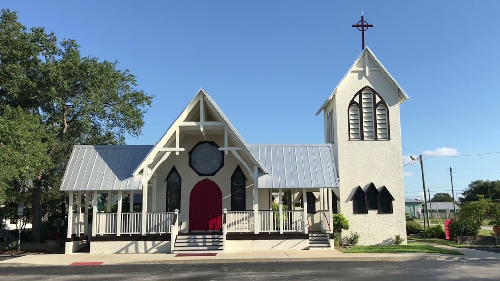 White community church with red entrance doors, front porch, and bell tower under a clear blue sky